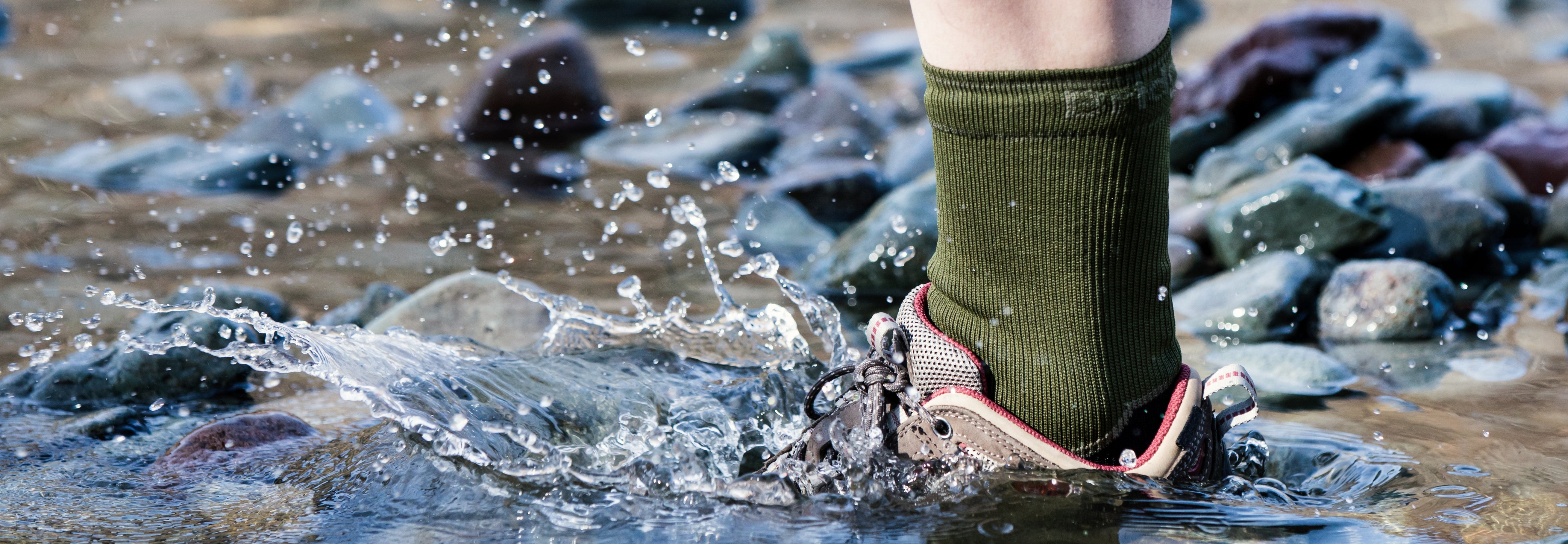 Person wearing green socks and red shoes stepping into a stream with water splashing around.