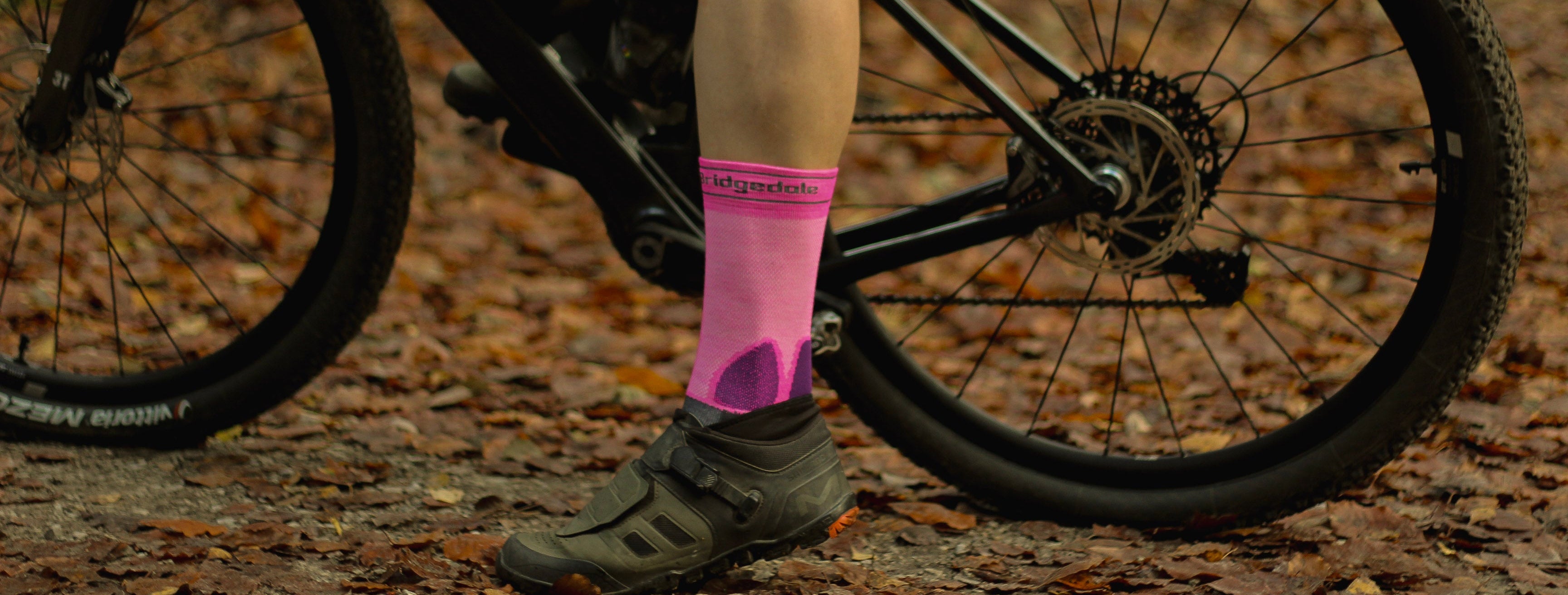 Person riding a bicycle on a trail wearing pink socks with visible branding.