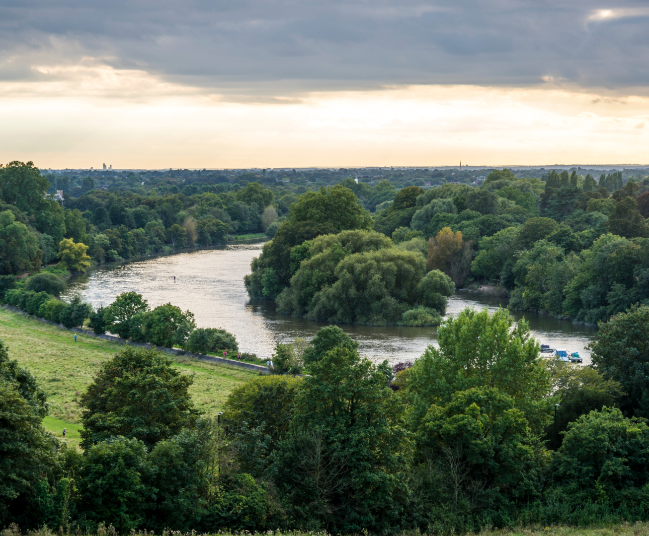 River flowing through a lush green landscape with trees and grass under a cloudy sky.Richmond Station to Ham House historic scenic walk, London